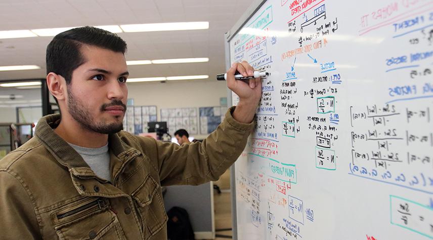A male student writing on a dry erase board to solve a mathematic problem